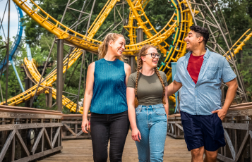 Group of three people on a bridge in front of a roller coaster