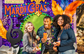 Three adults in front of a Mardi Gras sign